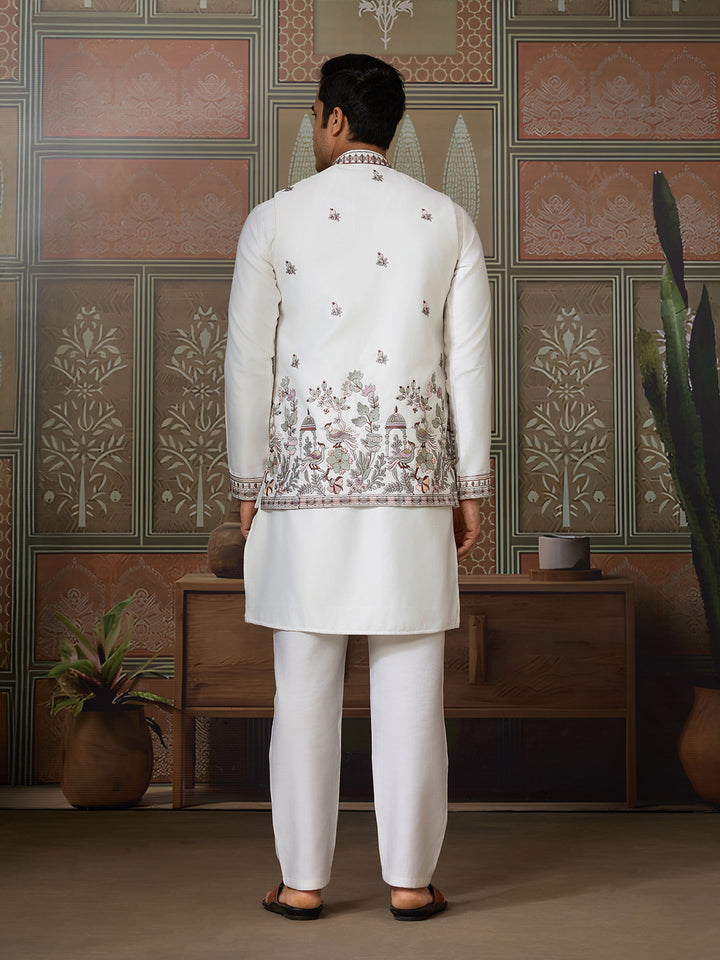 Man wearing a traditional white embroidered outfit in a decorated room.