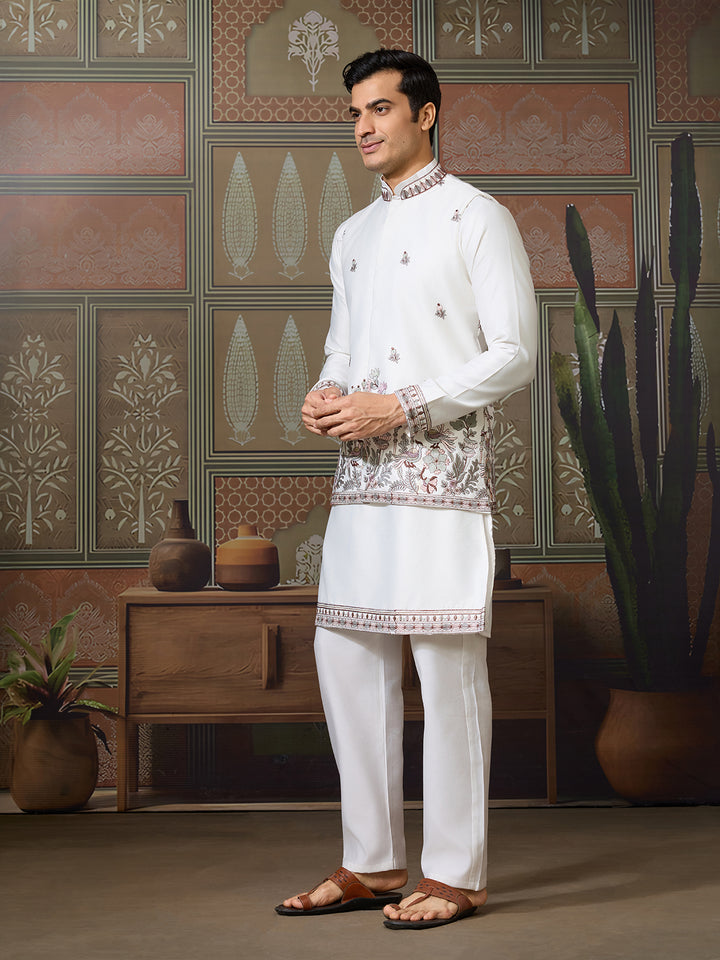 Man wearing a traditional white embroidered outfit in a decorated room.