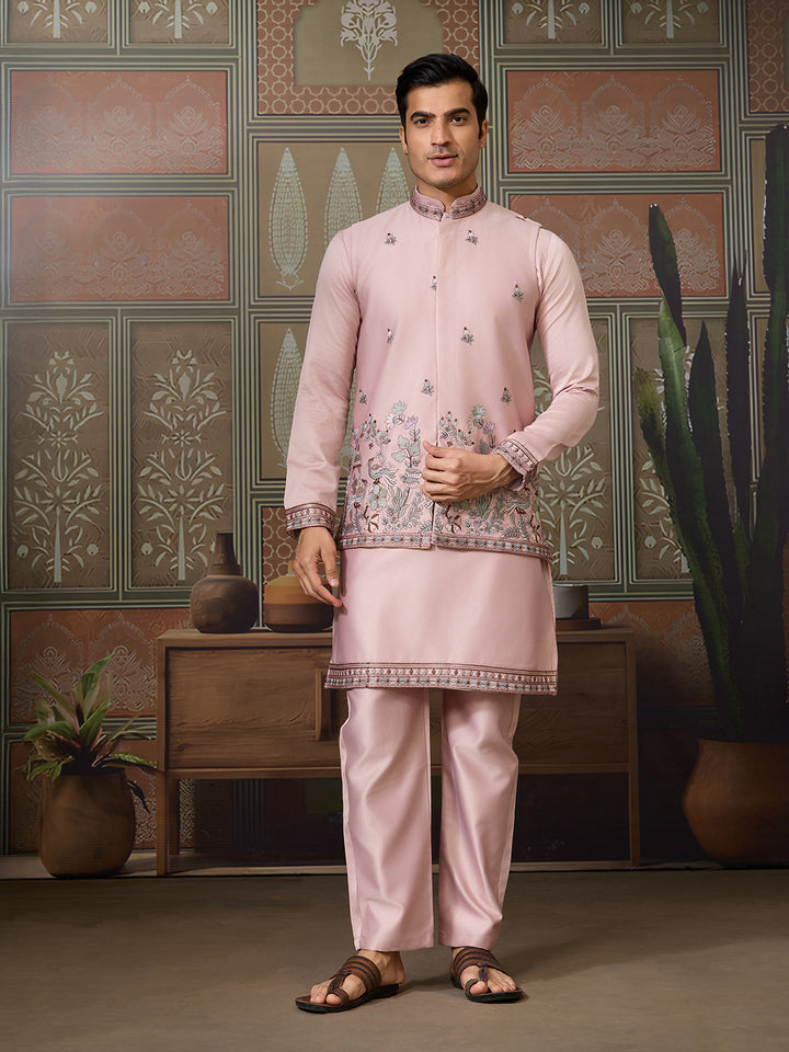 Man wearing a pink traditional outfit with intricate patterns in a decorative room.