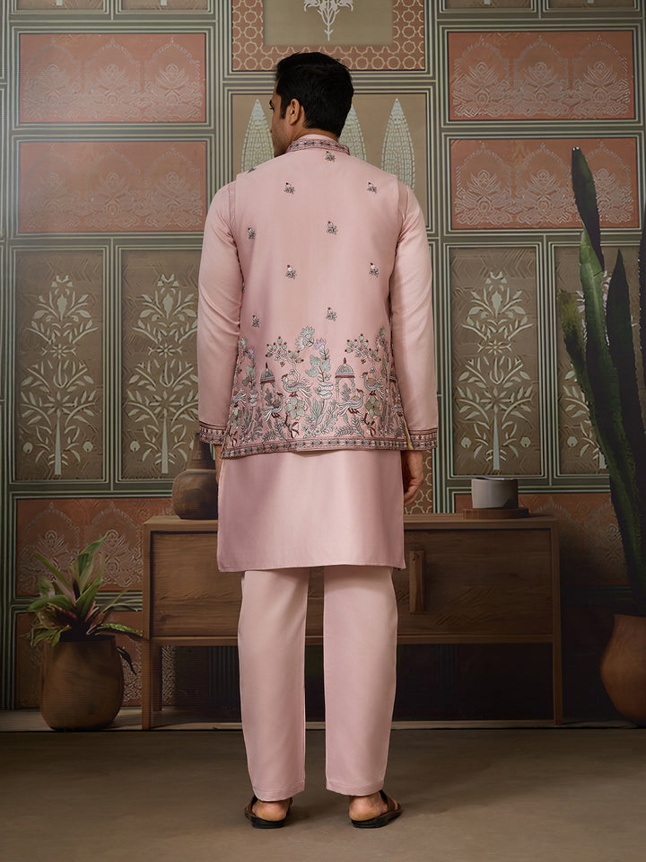Man wearing a pink embroidered traditional outfit standing in a room with decorative walls.