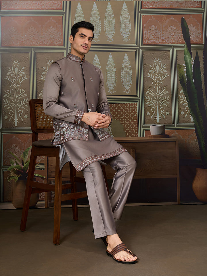 Man in traditional attire sitting on a chair against a patterned wall.