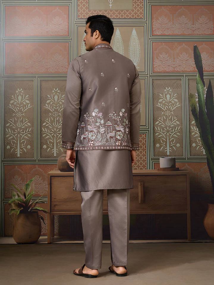 Man wearing a traditional embroidered outfit in a decorative room with patterned walls.