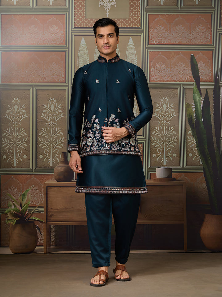 Man wearing a traditional embroidered outfit in a decorated room with patterned walls and plants.