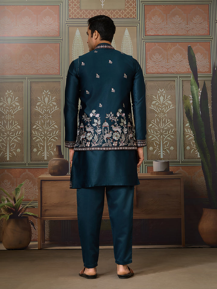 Man wearing a dark blue embroidered traditional outfit in a decorated room.