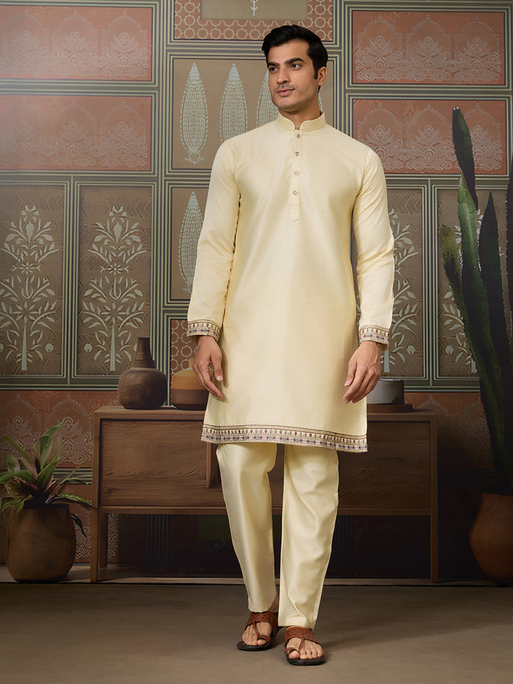 Man wearing a cream kurta with intricate patterns in a decorated room.