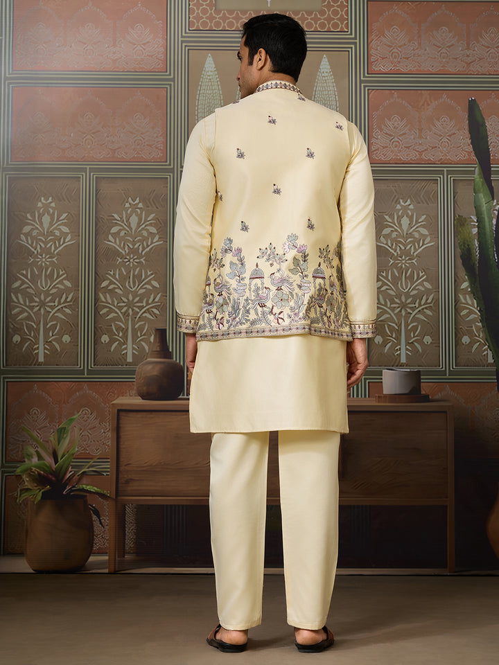 Man wearing a cream embroidered sherwani standing in a decorated room.