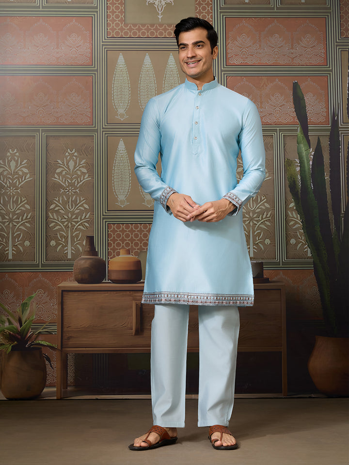 Man wearing a light blue kurta with white pants in a decorated room.