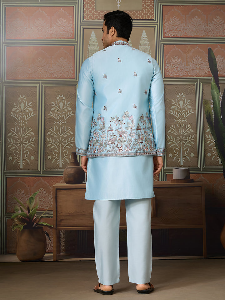 Man wearing a light blue embroidered traditional outfit in a decorated room.
