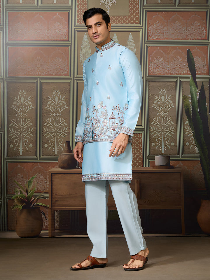 Man wearing a light blue embroidered traditional outfit in a decorated room.