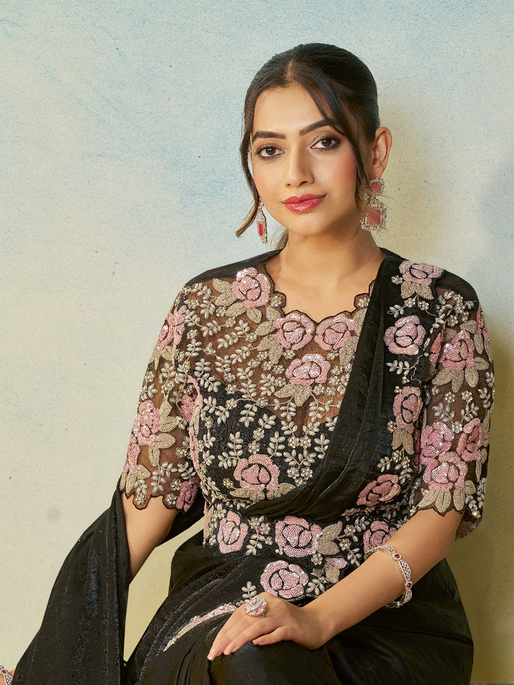 Woman wearing a black saree with floral patterns against a light background