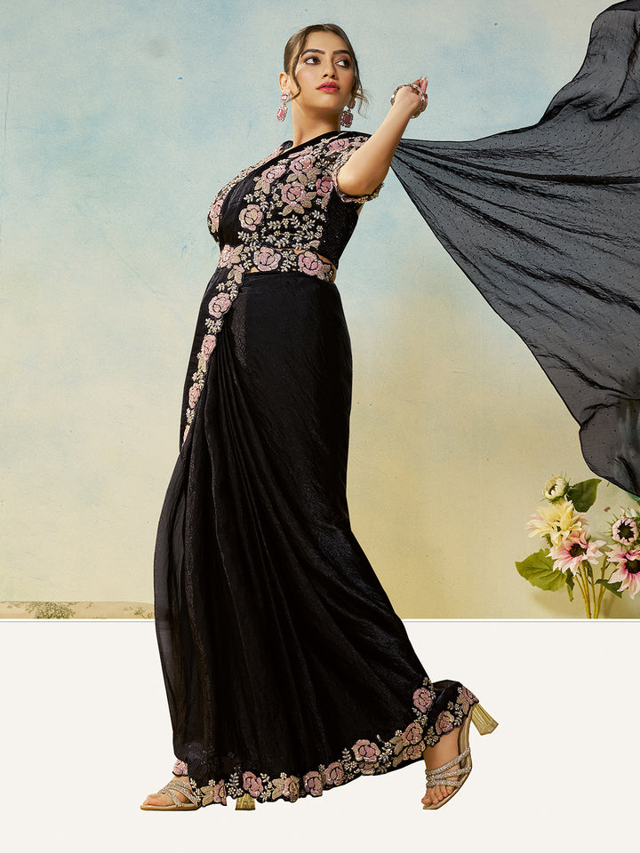 Woman in a black saree with floral embroidery holding a gray dupatta against a light background.