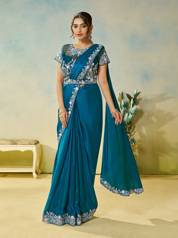 Woman wearing a blue saree with white embroidery in a room setting.