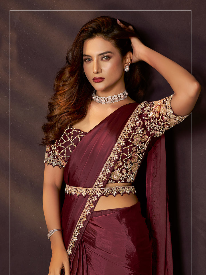 Woman in a maroon saree with gold embroidery against a dark background