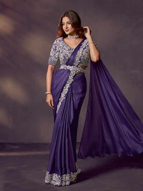 Woman wearing a purple saree with silver embroidery against a dark background