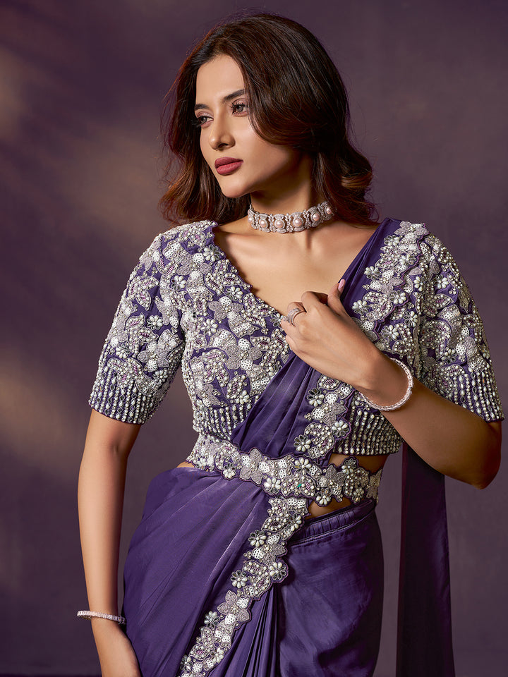Woman wearing a purple saree with silver embroidery against a dark background