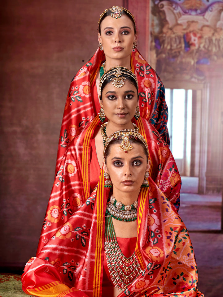 Three women in traditional red sarees with intricate patterns and jewelry against a warm-toned background.