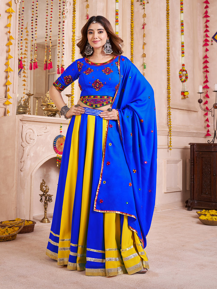 Woman wearing a blue and yellow traditional outfit in a decorated room.