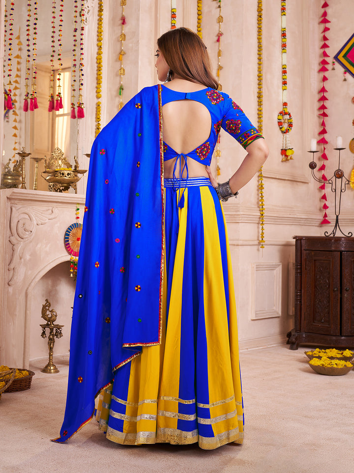 Woman wearing a blue and yellow traditional outfit in a decorated room.