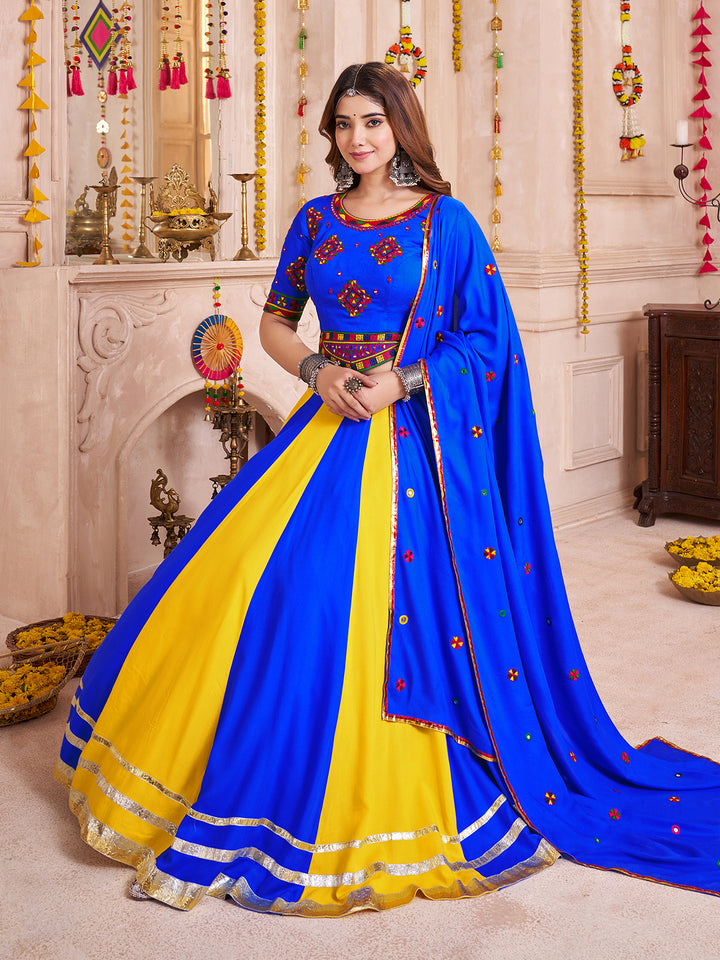 Woman wearing a blue and yellow saree with intricate designs in a decorated room.