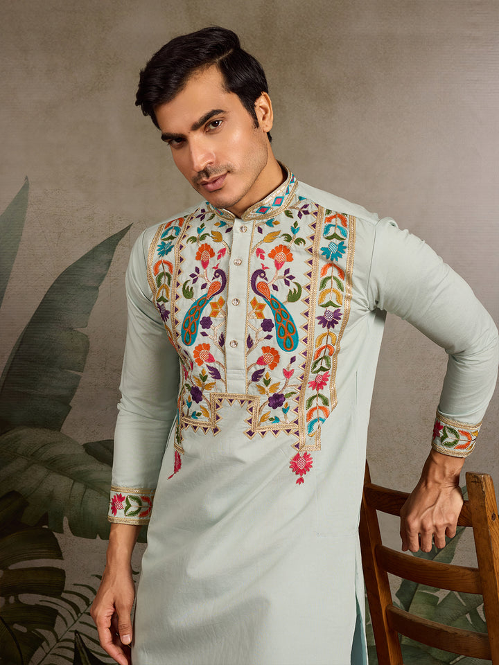 Man wearing a light blue kurta with colorful embroidery against a neutral background