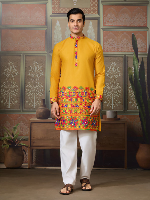 Man wearing a yellow kurta with colorful embroidery in a decorated room.
