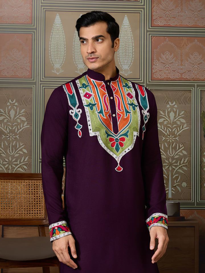 Man wearing a traditional embroidered kurta against a decorative wall.