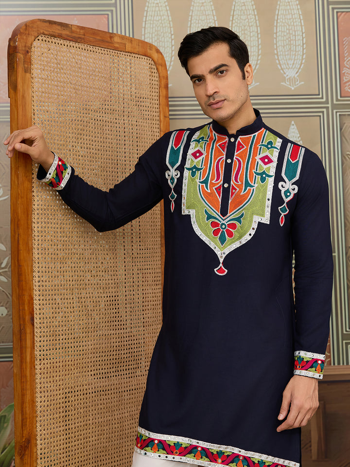 Man wearing a navy blue embroidered kurta standing against a decorative wall.