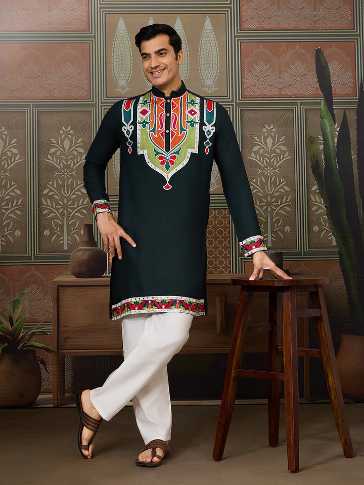 Man wearing a black embroidered kurta with white pants in a decorated room.