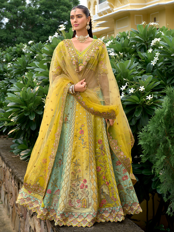 Woman in a yellow and green traditional outfit standing outdoors with greenery in the background