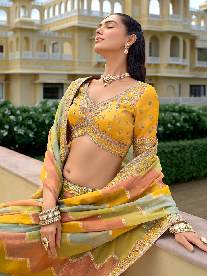 Woman in a yellow saree with intricate patterns in front of a building.