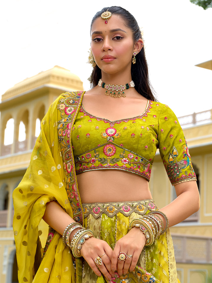 Woman in a traditional green and gold outfit with jewelry, standing in front of a building.