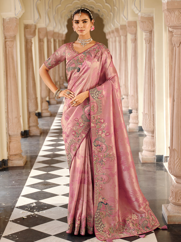 Woman in a pink saree with intricate designs standing in an elegant corridor.