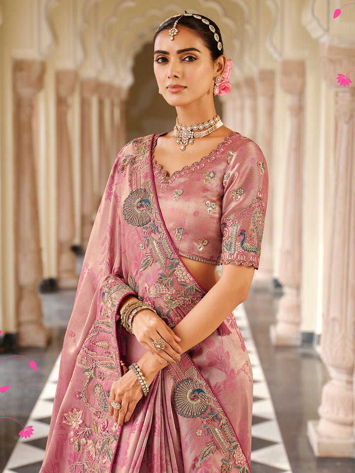 Woman in a traditional pink saree with intricate patterns in an elegant setting.