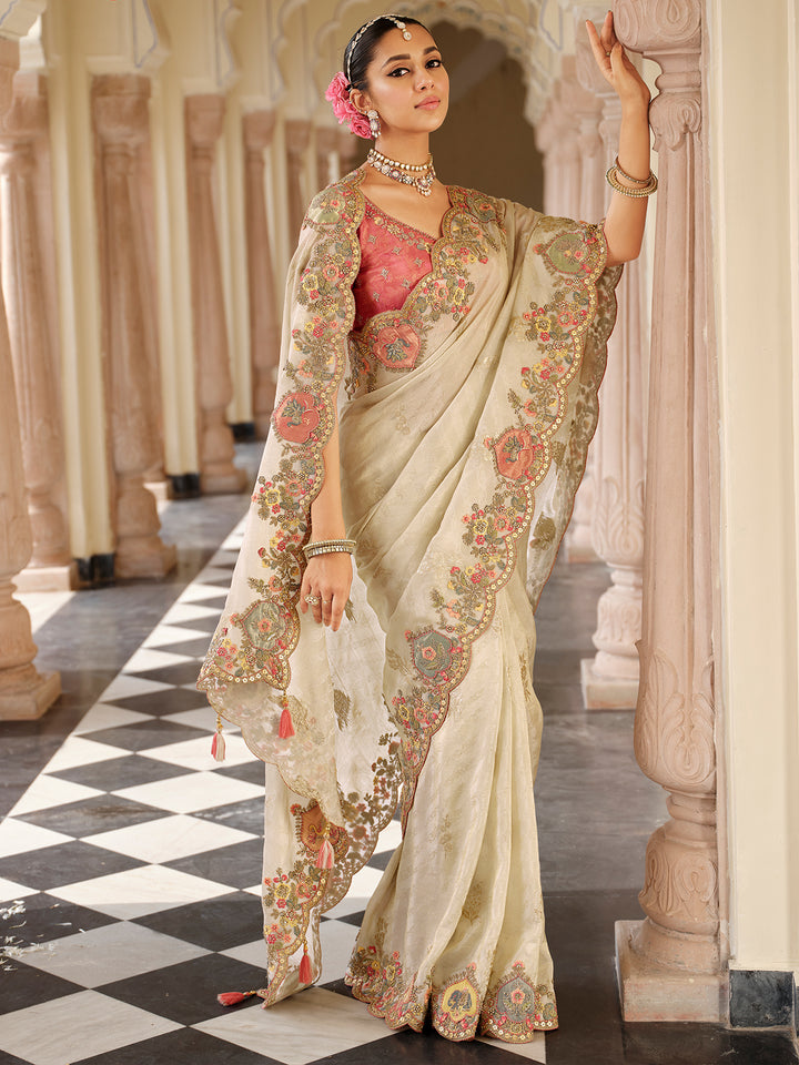 Woman in a traditional embroidered saree standing in an elegant interior setting.