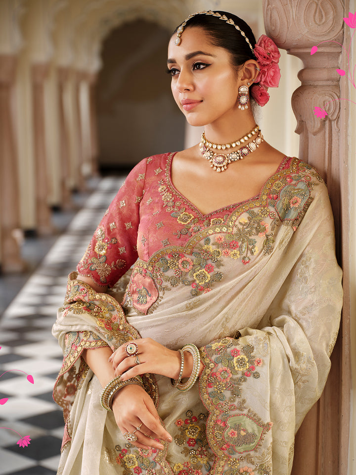 Woman in traditional embroidered saree with jewelry, standing against a decorative wall.