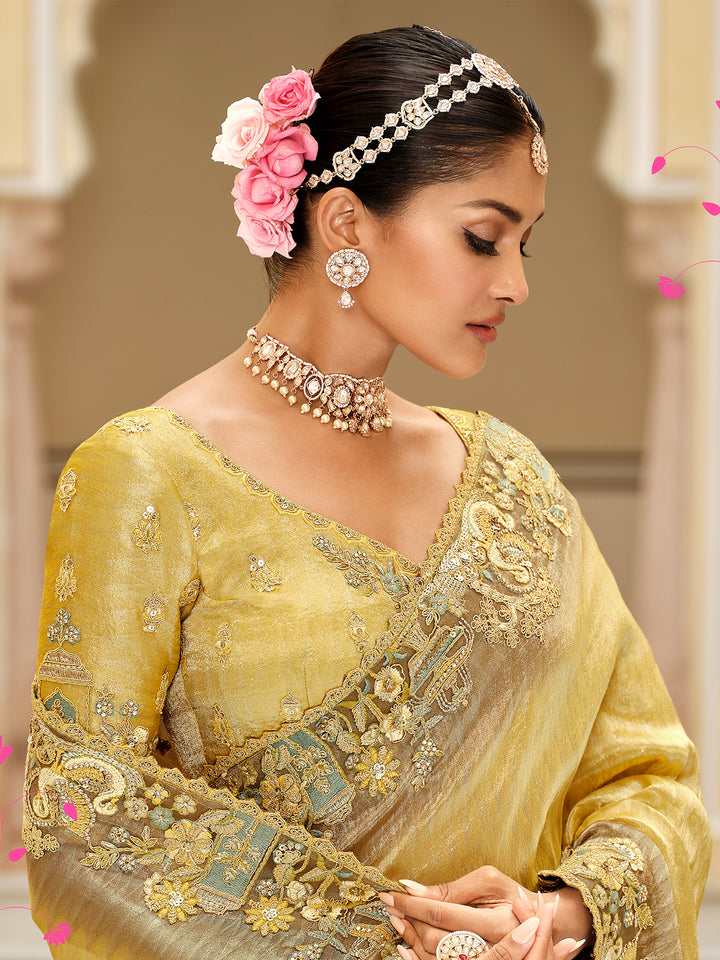 Woman in traditional yellow embroidered saree with jewelry and floral hair accessory.