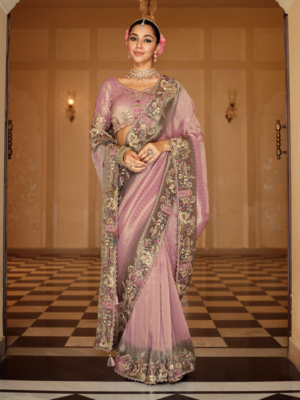 Woman in a traditional pink saree with intricate patterns in an elegant indoor setting.