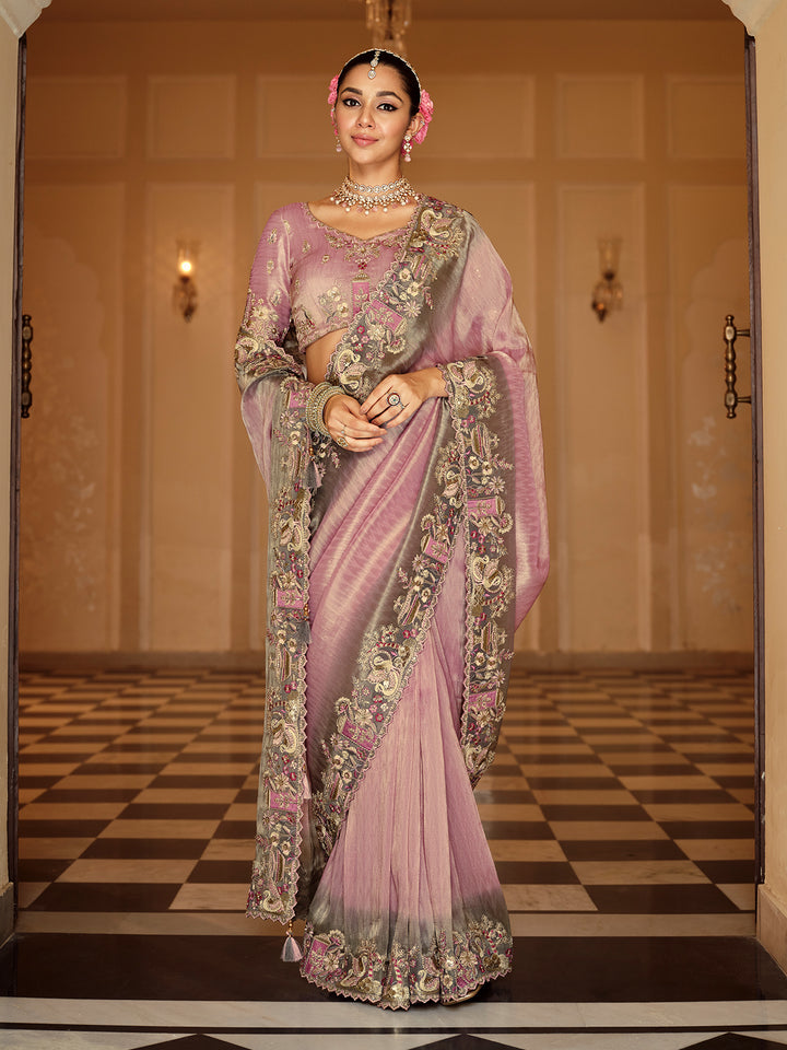 Woman in a traditional pink saree with intricate patterns in an elegant indoor setting.