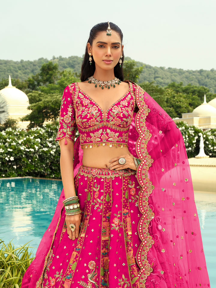 Woman in a traditional pink embroidered outfit standing by a pool with greenery in the background