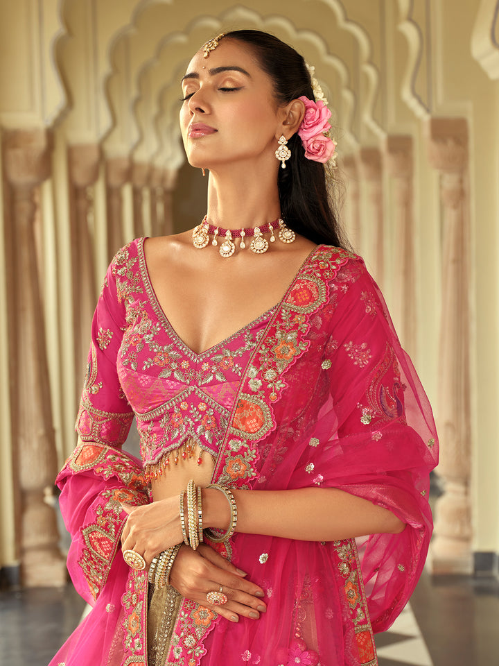 Woman in a traditional pink embroidered outfit with jewelry, standing against an architectural background.