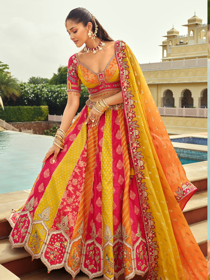 Woman in a vibrant pink and yellow traditional outfit with intricate patterns, standing by a pool with a building in the background.