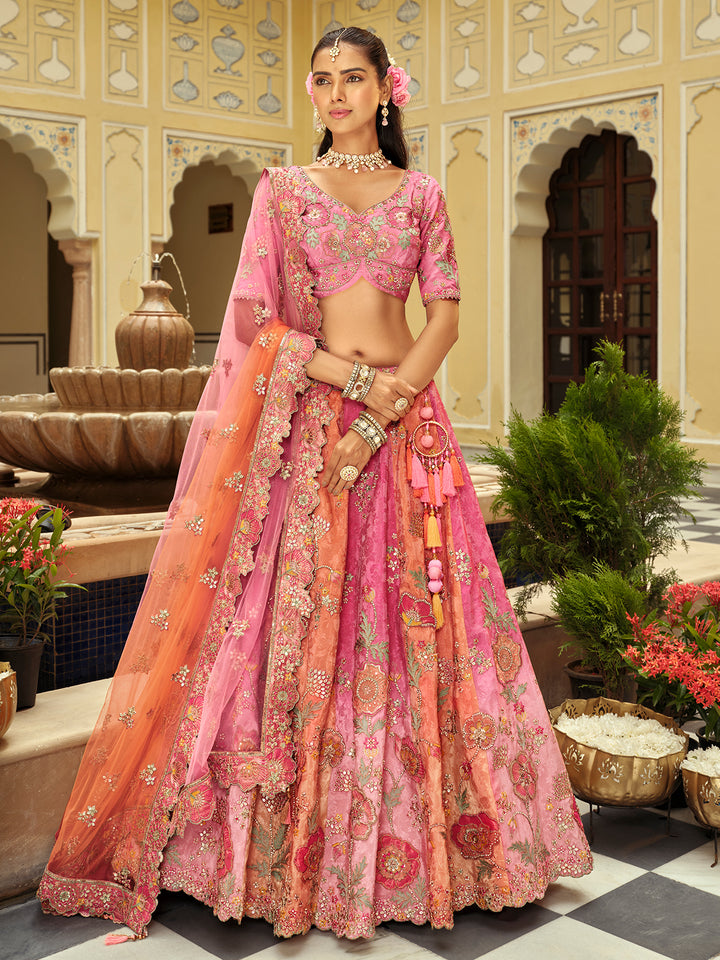 Woman in a traditional pink and orange embroidered outfit standing in an ornate courtyard.