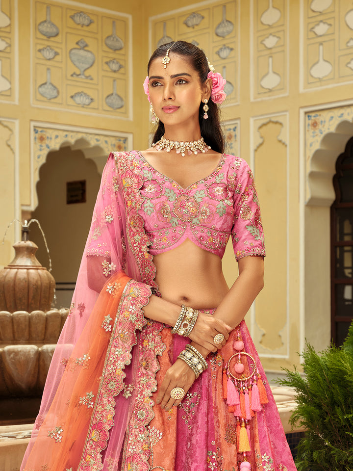 Woman in a traditional pink and orange embroidered outfit with jewelry in an ornate indoor setting.