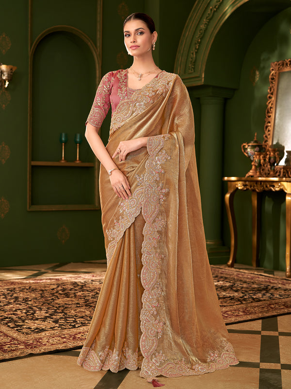 Woman in a beige saree with intricate designs in a decorative room.