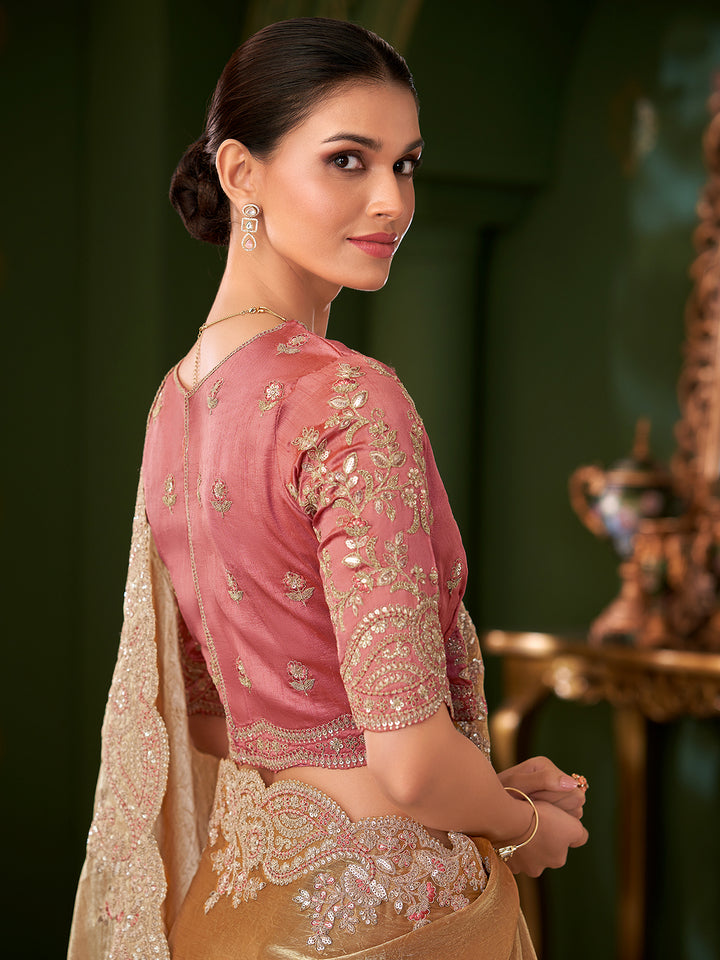 Woman wearing a traditional pink and gold blouse with a beige saree, against a dark green background.