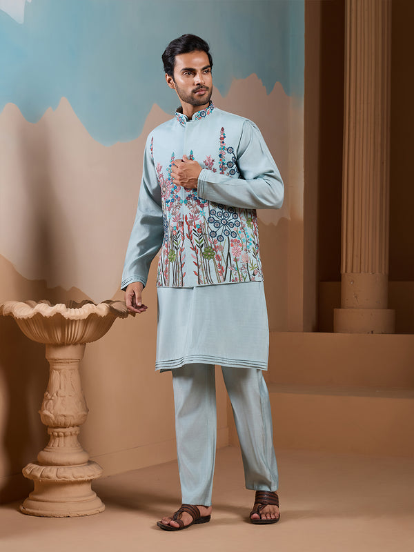 Man wearing a light blue traditional outfit with floral patterns in an indoor setting.