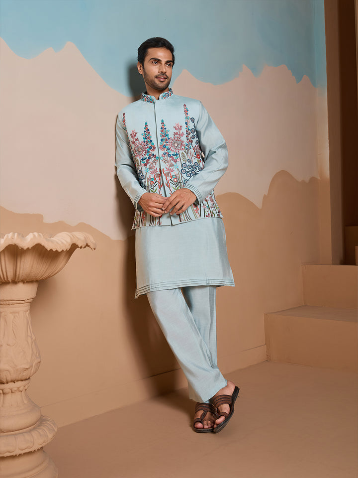 Man wearing a light blue embroidered traditional outfit in a decorative setting.