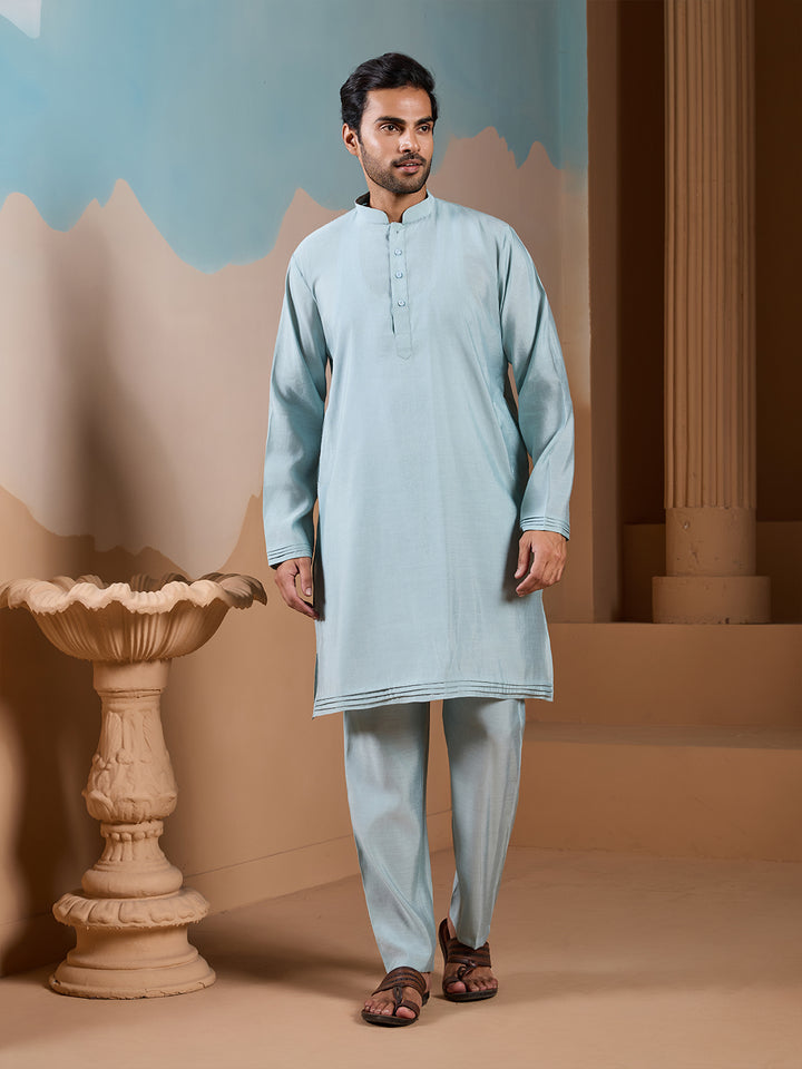 Man wearing a light blue kurta with pants standing in a decorative indoor setting.