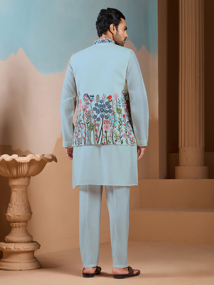 Man wearing a light blue traditional outfit with floral patterns in an indoor setting.