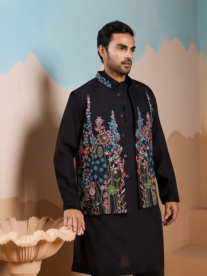 Man wearing a black embroidered traditional outfit against a decorative background